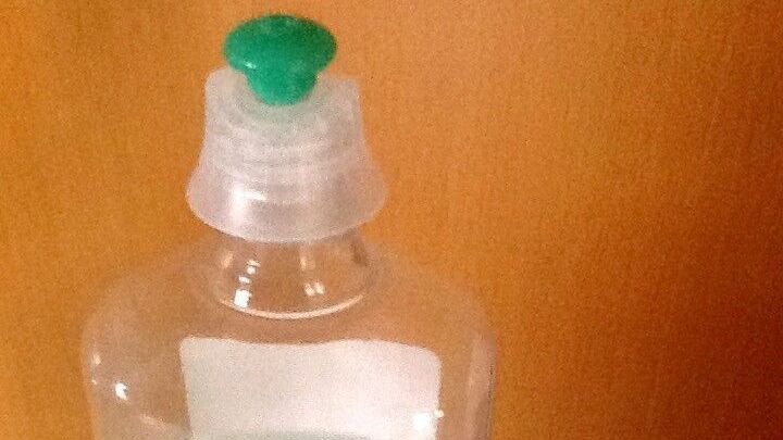 Eine Flasche Neutralreiniger steht auf einer Oberfl&auml;che, w&auml;hrend die gr&uuml;ne Verschlusskappe daneben liegt, bereit zum Austausch.