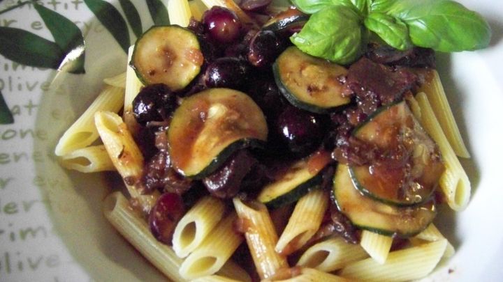 Ein k&ouml;stliches Rehragout mit Trauben und Zucchini liegt auf einer Portion Penne, garniert mit frischem Basilikum.