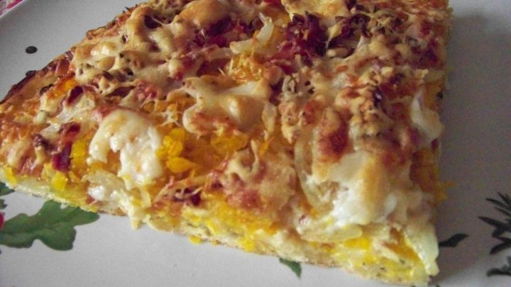 Eine k&ouml;stliche K&uuml;rbispizza mit Ziegenk&auml;se und Parmesan liegt auf einem rustikalen Teller, umgeben von pflanzlichem Dekor.