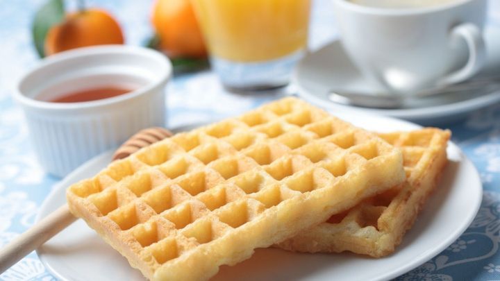 Waffeln mit nat&uuml;rlichem Fruchtaroma liegen auf einem Teller, umgeben von orangefarbenem Saft und einer Tasse Kaffee.