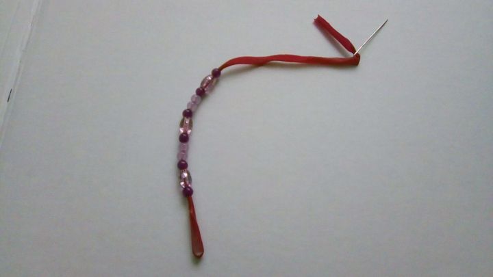 Ein rotes Gummiband mit bunten Perlen ist zu einem Armband geflochten, auf einem wei&szlig;en Untergrund liegend.