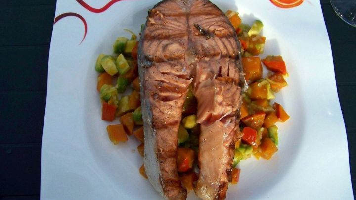 Ein gegrilltes Lachssteak liegt saftig auf einem bunten Avocado-Bett, umgeben von frischen Gem&uuml;sew&uuml;rfeln.
