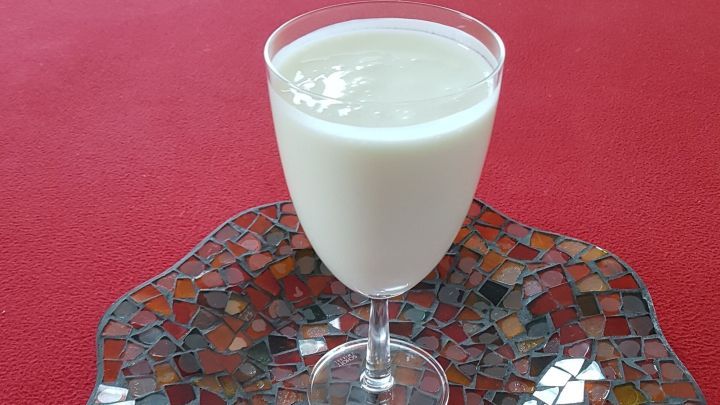 Ein Glas Buttermilch steht auf einem bunten Teller auf einem roten Tisch, bereit zum Trinken und Abnehmen.