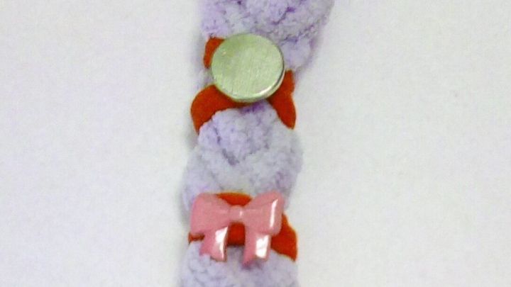 Ein geflochtener, haarschonender Zopfgummi ist dekoriert mit bunten Kn&ouml;pfen und Figuren, liegt auf einem wei&szlig;en Hintergrund.