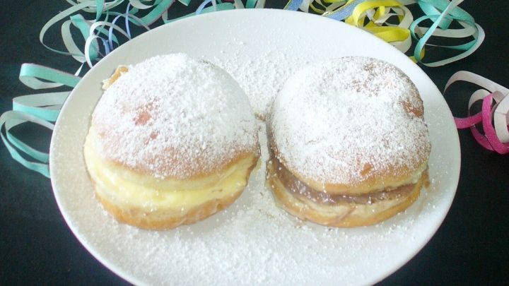 Zwei gef&uuml;llte Berliner auf einem wei&szlig;en Teller, umgeben von bunten Konfetti-R&ouml;llchen, die festliche Stimmung vermitteln.