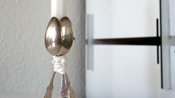 Ein Kerzenst&auml;nder aus Omas altem Silberbesteck steht elegant auf einem wei&szlig;en Tisch und h&auml;lt eine d&uuml;nne, wei&szlig;e Kerze.