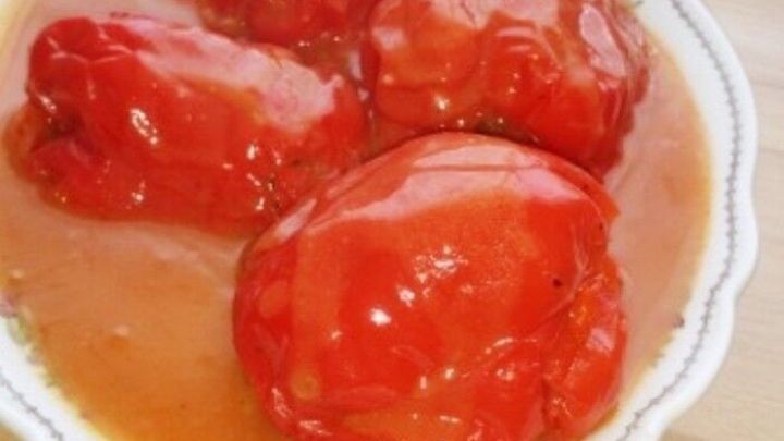 Gef&uuml;llte Paprika liegen in einer wei&szlig;en Sch&uuml;ssel in einer schmackhaften Tomatensauce auf einem Holzuntergrund.