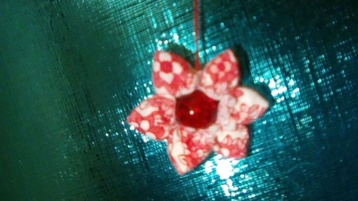 Eine dekorative, rote Stoffblume h&auml;ngt an einem Faden vor einem glanzvollen, gr&uuml;nen Hintergrund.