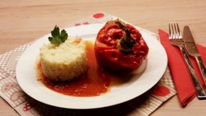 Gef&uuml;llte Paprikaschoten liegen auf einem Teller neben einem gef&auml;hrten aus Reis, serviert in einer gem&uuml;tlichen K&uuml;che.