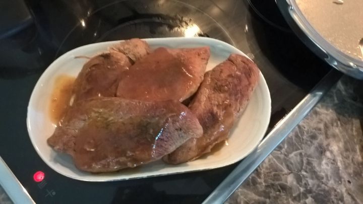 Saftige Putenbrust liegt auf einem wei&szlig;en Teller im K&uuml;chenumfeld, frisch aus dem Schnellkochtopf.