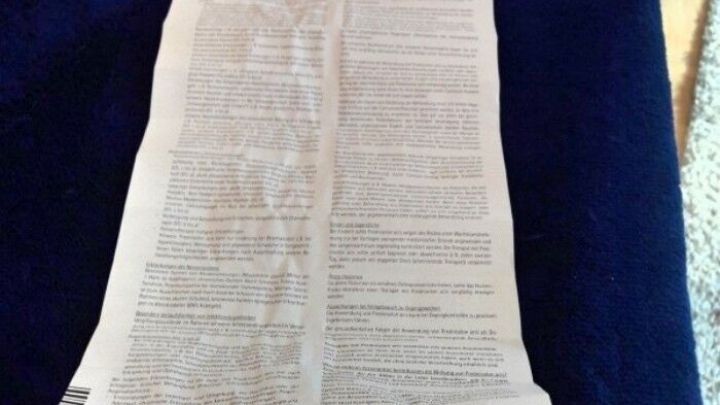 Ein langer, gefalteter Beipackzettel liegt auf einem blauen Untergrund und enth&auml;lt dichte, kleine Schrift.