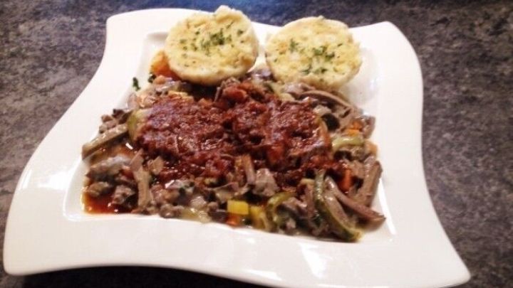 Ein gro&szlig;z&uuml;gig angerichteter Teller zeigt Wiener Salonbeuschel mit dunkler Sauce und Kn&ouml;deln, auf einer eleganten wei&szlig;en Servierplatte.