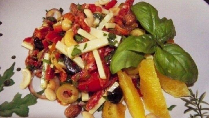 Ein bunter Wurstsalat liegt auf einem Teller, gemischt mit frischem Gem&uuml;se, angerichtet mit Basilikum und Orange.