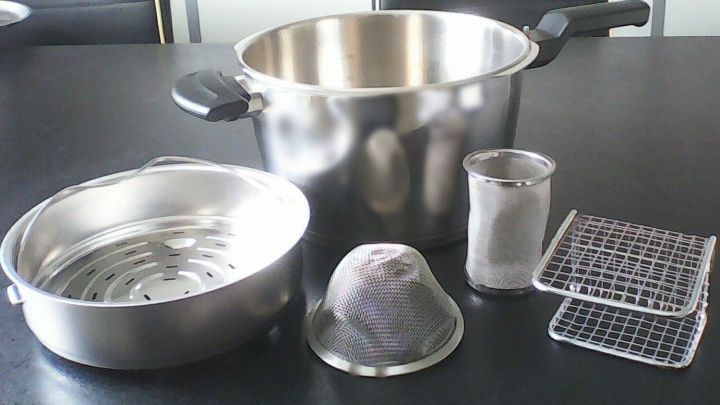 Ein Schnellkochtopf mit verschiedenen Alternativ-St&auml;ndern und Siebeins&auml;tzen liegt auf einem Tisch und ist bereit zum Kochen.