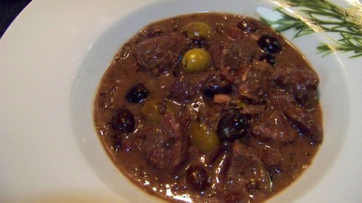 Ein Schmortopf mit zartem Fleisch, Oliven und Trockenfr&uuml;chten in einer reichhaltigen Sauce, serviert auf einem wei&szlig;en Teller.