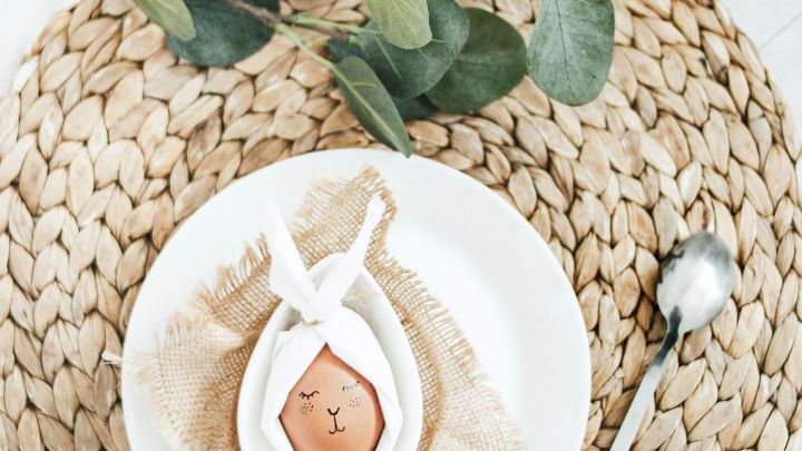 Ein dekorierter Tisch mit einem Servietten-Osterhasen auf einem wei&szlig;en Teller, umgeben von nat&uuml;rlicher Tischw&auml;sche und einem L&ouml;ffel.