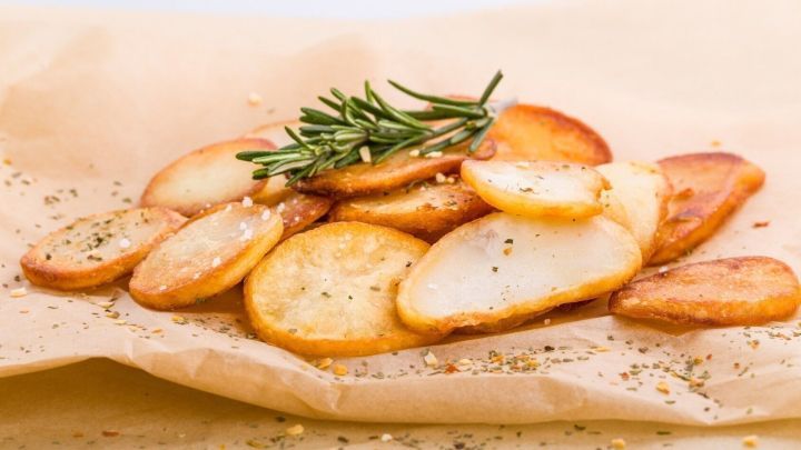 Knusprige Bratkartoffeln liegen auf braunem Papier, garniert mit Rosmarin und leicht gepfeffert, appetitlich angerichtet.
