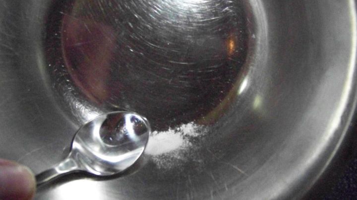 Eine S&uuml;&szlig;stofftablette wird mit einem L&ouml;ffel in einer gl&auml;nzenden Sch&uuml;ssel zerdr&uuml;ckt, um sie aufzul&ouml;sen.