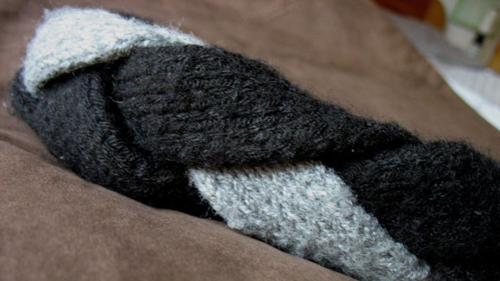 Ein selbst gestricktes Stirnband liegt geschickt geflochten auf einem braunen Stoff, bereit zum Tragen.