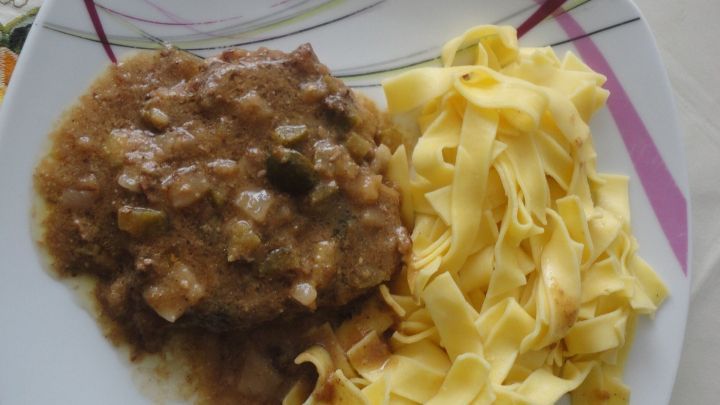 Ein saftiges Rindsschnitzel liegt neben zarten Bandnudeln auf einem dekorativen Teller in einer hellen Umgebung.