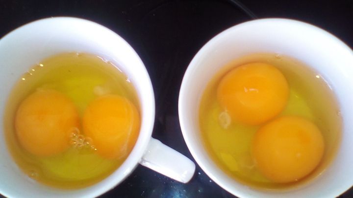 Zwei Tassen mit frischen Eiern stehen auf einer Arbeitsfl&auml;che, w&auml;hrend die Eier aufgeschlagen und bereit zum Kochen sind.