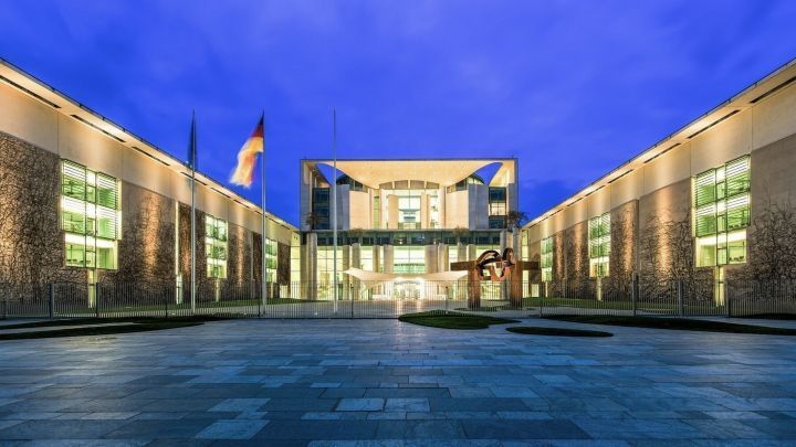 Ein modernes Geb&auml;ude mit Glasfassade steht im Zentrum, umgeben von einem klaren Abendhimmel und einer gepflasterten Fl&auml;che.