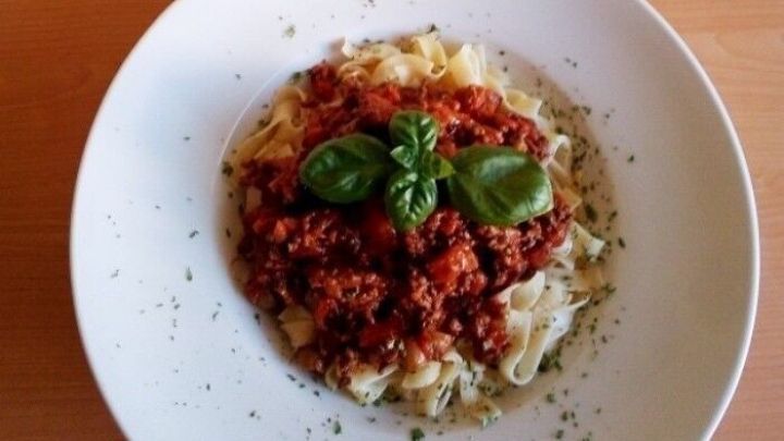 Zwei Teller mit Bandnudeln sind mit einer &uuml;ppigen Bolognese-Sauce und frischem Basilikum garniert, auf einem Holztisch.