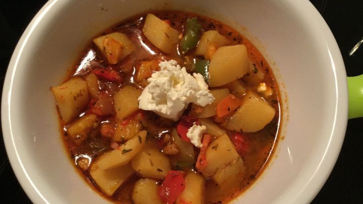 Ein bunter Teller Kartoffelgulasch mit weichen Kartoffeln und einem Klecks Creme in einer wei&szlig;en Sch&uuml;ssel.