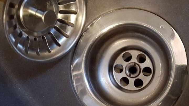 Ein Abflusssieb liegt neben einem Waschbecken. Es wird gereinigt, um Verstopfungen zu vermeiden und den Wasserfluss zu sichern.