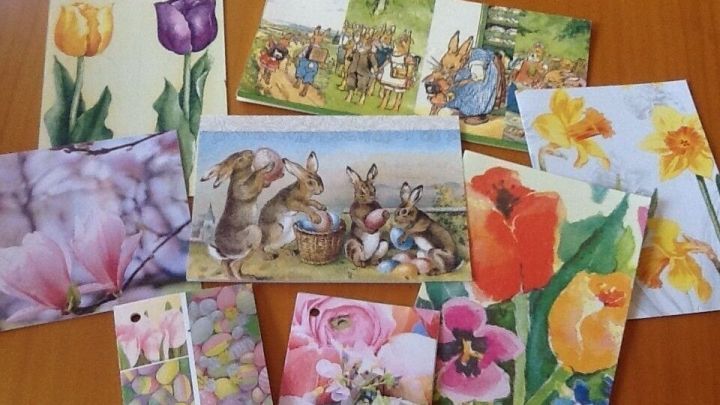 Bunte Gru&szlig;karten aus Servietten liegen auf einem Tisch und zeigen vielf&auml;ltige Fr&uuml;hlingsmotive mit Blumen und Tieren.