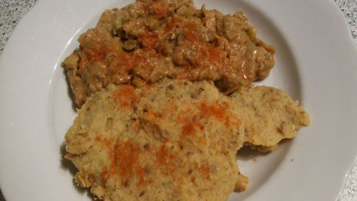 Auf einem wei&szlig;en Teller sind zwei Portionen zu sehen: eine Mischung aus kleinem, gelblichem Brot oder Teig und eine scharfe Erdnussso&szlig;e, die neben der dicken, cremigen Sauce pr&auml;sentiert wird.