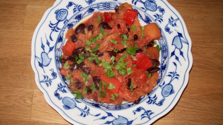 Ein bunter Bauerntopf ohne Fleisch liegt appetitlich in einer wei&szlig;en Sch&uuml;ssel mit blauen Rankenmustern auf einem Holztisch.