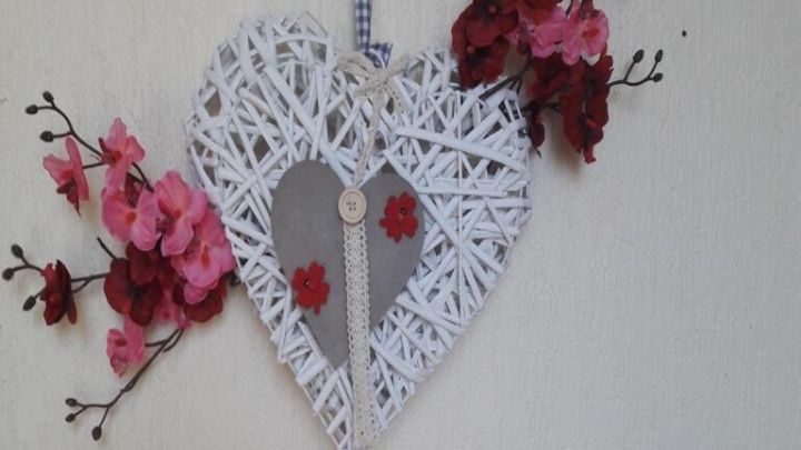 Ein herzf&ouml;rmiger Kranz aus wei&szlig;en Ranken h&auml;ngt an einer Wand, umgeben von rosa Blumen, perfekt f&uuml;r die Osterdekoration.