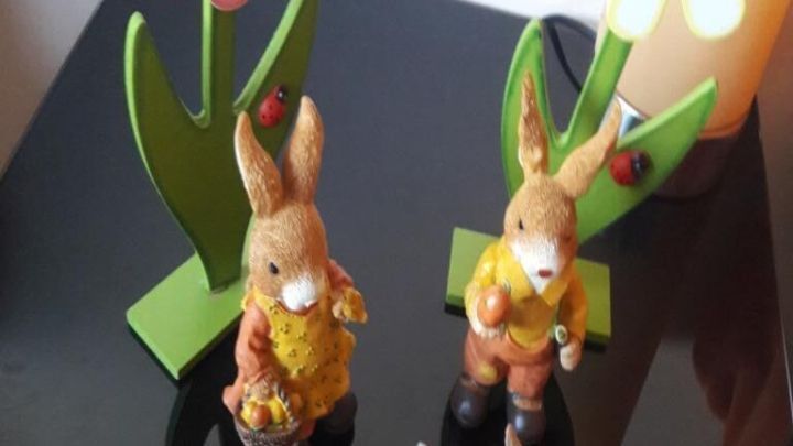 Drei dekorative Osterhasen stehen vor bunten Blumen auf einem Tisch, passend zur festlichen Osterzeit.