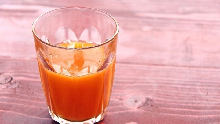 Ein Glas Karottensaft steht auf einer rustikalen Holzoberfl&auml;che und reflektiert sanft das Licht, das den Saft erleuchtet.