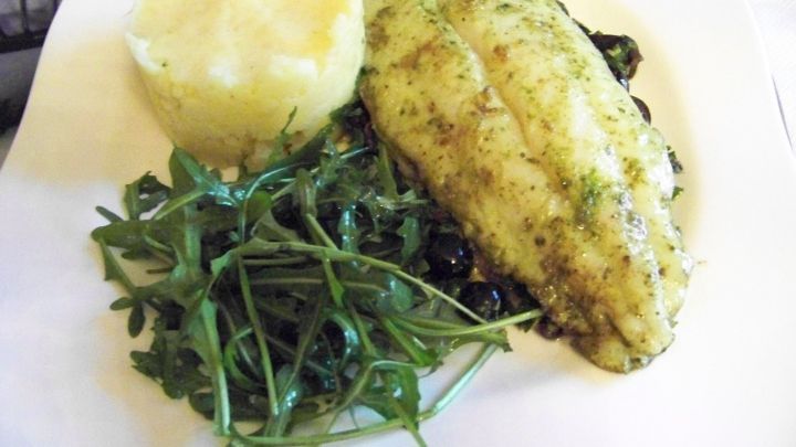 Ein gegrillter Fisch liegt auf einem Bett aus Oliven, garniert mit frischem Rucola und cremigem Kartoffelp&uuml;ree.