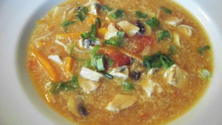 Eine k&ouml;stliche Pekingsuppe in einer wei&szlig;en Sch&uuml;ssel, gef&uuml;llt mit buntem Gem&uuml;se und zarten H&uuml;hnerst&uuml;ckchen.