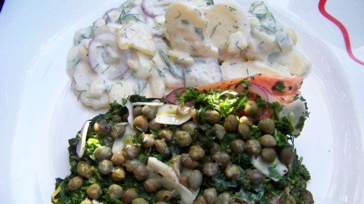 Ein gegrilltes Lachsfilet ist mit einer Kr&auml;uterhaube und einem gr&uuml;nen Salat belegt, serviert auf einem wei&szlig;en Teller.