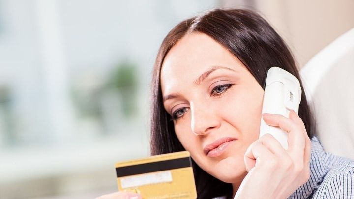 Eine Frau sitzt am Computer und telefoniert, w&auml;hrend sie eine Kreditkarte in der Hand h&auml;lt, bereit zum Online-Kauf.