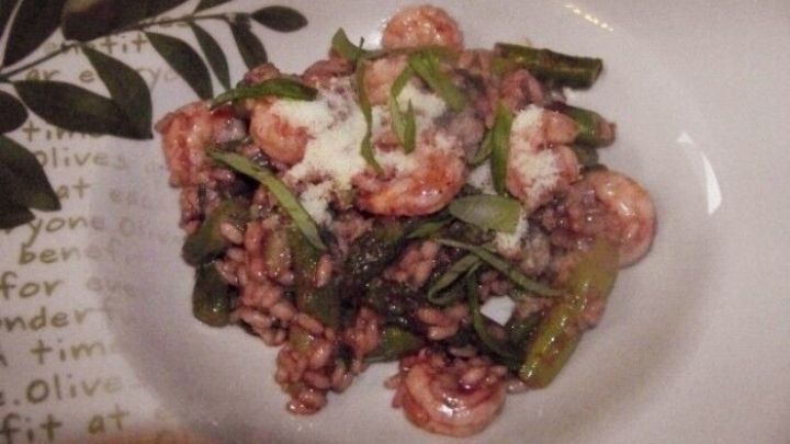 Ein cremiges Risotto mit Spargel und Garnelen liegt auf einem dekorierten Teller, umgeben von gr&uuml;nem Gem&uuml;se.