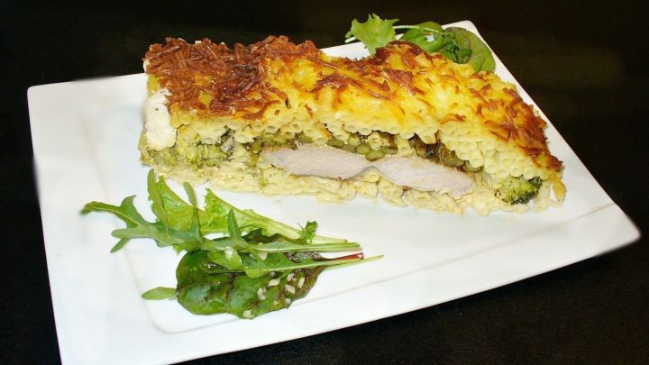 Ein knuspriger Auflauf aus Makkaroni und Filetspitzen mit gr&uuml;nem Spargel auf einem wei&szlig;en Teller, garniert mit Rucola.