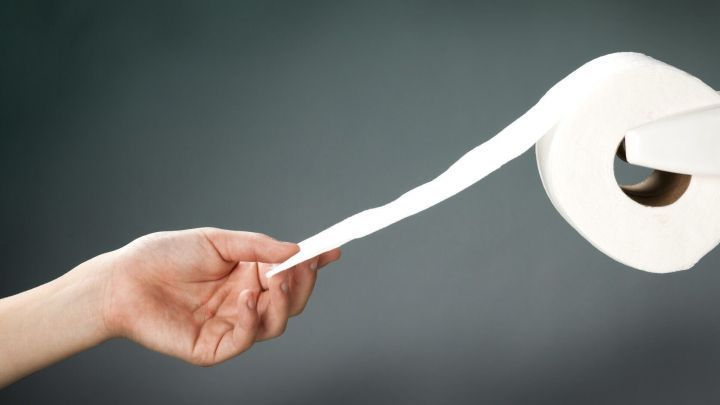 Eine Hand h&auml;lt ein St&uuml;ck Toilettenpapier, w&auml;hrend es von einer Rolle abgerollt wird. Hygiene auf der Toilette ist wichtig.