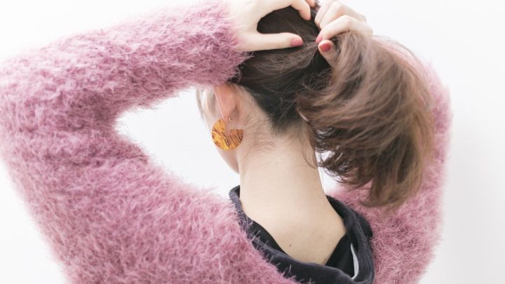 Eine Person mit einem flauschigen rosa Pullover bindet ihre Haare zu einem Pferdeschwanz, um schnell einen Haargummi zu ersetzen.