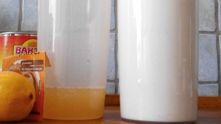 Ein Glas mit Kichererbsenwasser steht neben einem Glas mit schaumigem Eischnee-Ersatz, umgeben von einer Zitrone und einem Saftkarton.