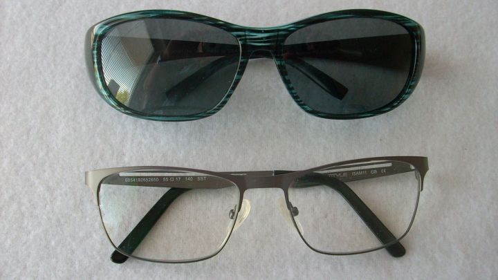 Eine Sonnen&uuml;berbrille liegt oben auf einer Gleitsichtbrille. Beide Brillen sind auf einem hellen, neutralen Untergrund positioniert.