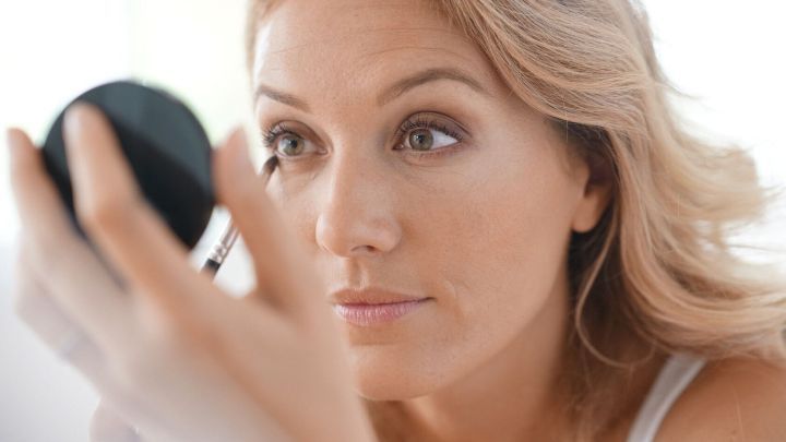 Eine Frau betrachtet sich im Spiegel, w&auml;hrend sie Kajal auf der Wasserlinie auftr&auml;gt. Nat&uuml;rliches Licht umgibt sie.