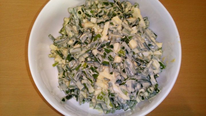 Ein frischer Schnittlauchsalat liegt in einer wei&szlig;en Sch&uuml;ssel, umgeben von einer holzfarbenen Tischoberfl&auml;che.