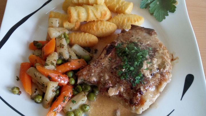 Gef&uuml;llte Schweinekoteletts liegen auf einem wei&szlig;en Teller, umgeben von Nudelspiralen und buntem Gem&uuml;se.