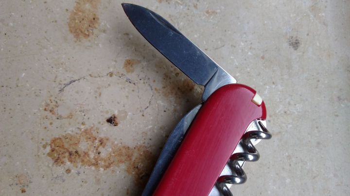 Ein rotes Taschenmesser liegt auf einem grauen Untergrund, w&auml;hrend die Klinge und der Korkenzieher sichtbar sind.