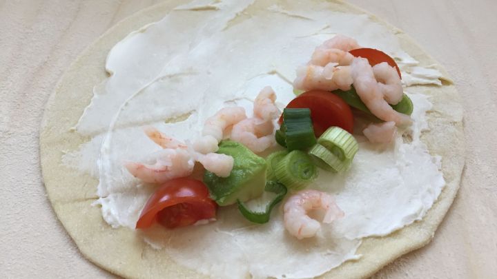 Eine Quesadilla wird mit Frischk&auml;se, Tomaten, Fr&uuml;hlingszwiebeln und Garnelen gef&uuml;llt und liegt auf einer Holzoberfl&auml;che.